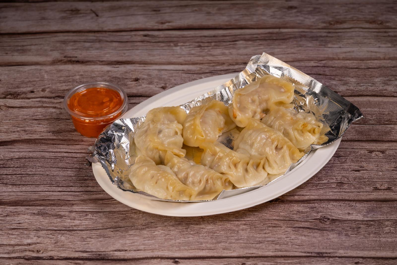 Steamed momos on foil with a side of red chili sauce